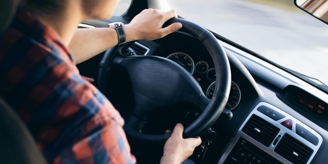 Close-up view of a man driving a modern car, showing dashboard and steering details.
